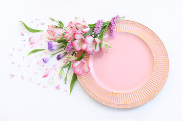 Top view of vintage white empty plate over spring flowers. Flat lay