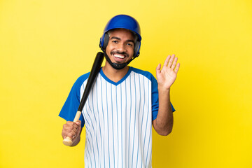 Young Colombian latin man playing baseball isolated on yellow background saluting with hand with happy expression