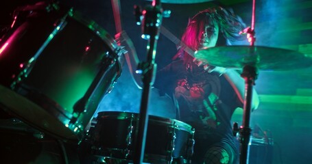 Young beautiful girl playing drums on the stage of nightclub