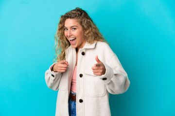 Young blonde woman isolated on blue background surprised and pointing front