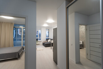 Small and white apartment corridor with many white doors and black door handles, wooden floor and bedroom doors open