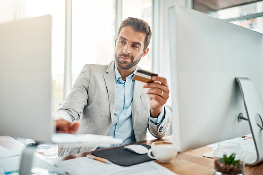 The Ease Of Online Banking. Shot Of A Handsome Young Businessman Using A Computer While Holding A Credit Card In An Office.