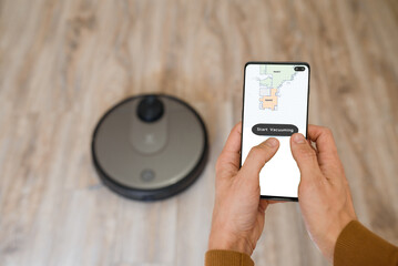 holding a smartphone and start vacuuming on robotic vacuum cleaner.