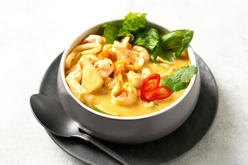 Asian laksa soup with shrimp in a ceramic bowl on a light culinary background. Spicy broth soup with coconut milk, rice noodles and seafood in a plate on the closeup kitchen table closeup
