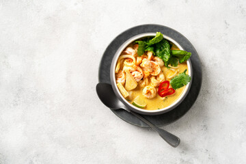 Asian laksa soup with shrimp in a ceramic bowl on a light culinary background. Spicy broth soup with coconut milk, rice noodles and seafood in a plate on the closeup kitchen table. Top view