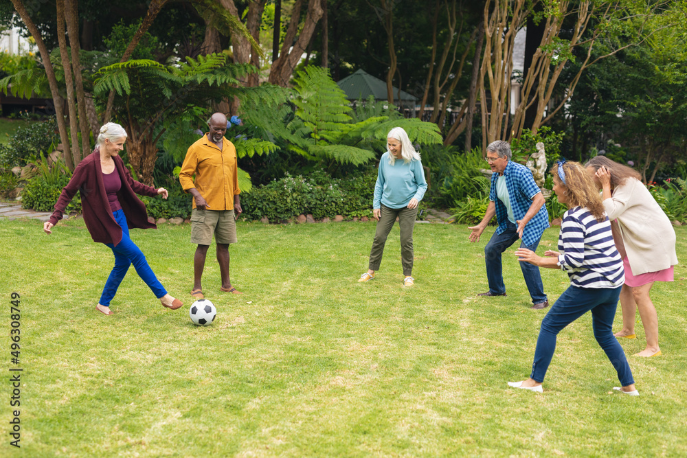 Wall mural multiracial active senior male and female friends playing soccer in backyard