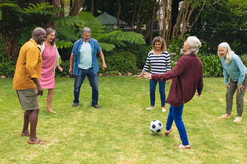 Multiracial active senior male and female friends playing soccer together in backyard on weekend