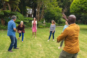Fototapeta premium Multiracial active senior male and female friends playing rugby in backyard on weekend