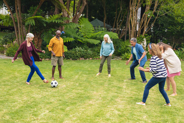 Multiracial active senior male and female friends playing soccer in backyard