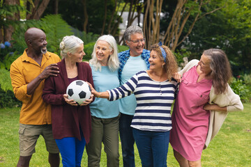 Happy multiracial active senior male and female friends with soccer ball in backyard