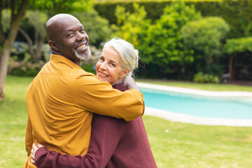 Portrait of happy multiracial senior couple looking over shoulders in backyard