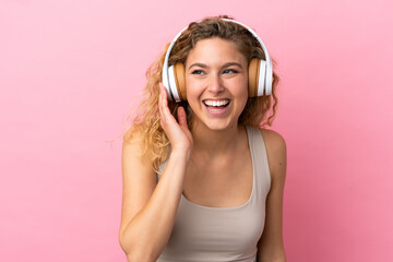 Young blonde woman isolated on pink background listening music