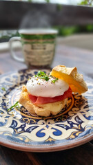 breakfast with egg pouché slice of ham on a cheese bread close-up with blurred coffee cup