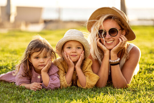 Beautiful photo of cute happy little sisters playing with her mother outside. Woman and her daughters lying on the green grass in the park. Happy family. Happy Mother's Day.