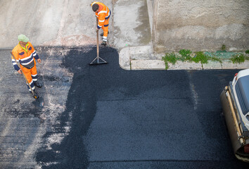 worker leveling fresh asphalt during asphalt pavement repair or construction works - obrazy, fototapety, plakaty