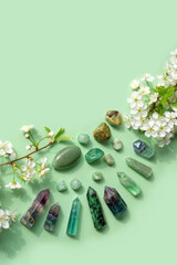 Gemstones minerals set of green colors and white cherry flowers on green background. Healing stones for Crystal Ritual, Esoteric spiritual practice. modern wicca magic. top view