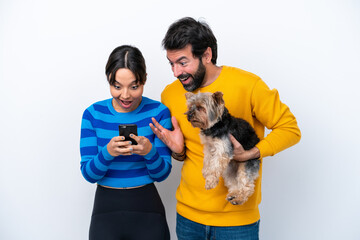 Young hispanic woman holding a dog isolated on white background sending a message or email with the mobile