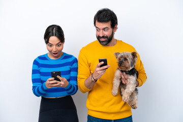 Young hispanic woman holding a dog isolated on white background Surprised and sending a message or email with the mobile