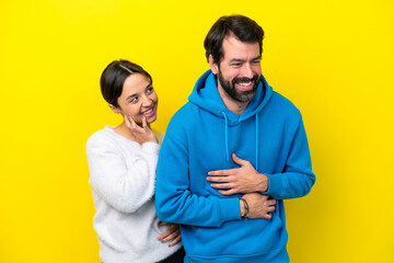 Young caucasian couple isolated on yellow background smiling a lot