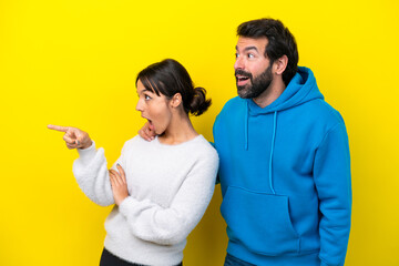 Young caucasian couple isolated on yellow background presenting an idea while looking smiling towards