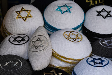 Stacks of white and black knit yarmulkes stitched with a Jewish star in the center on a table...