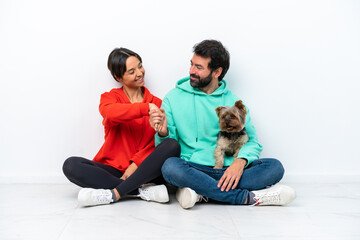 Fototapeta na wymiar Young caucasian couple sitting on the floor with their pet isolated on white background handshaking after good deal