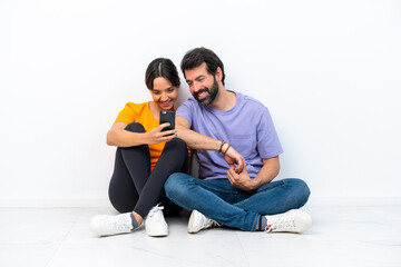 Fototapeta na wymiar Young caucasian couple sitting on the floor isolated on white background sending a message or email with the mobile