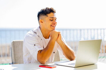 Happy argentinian student sinning with laptop outdoors and looking glad