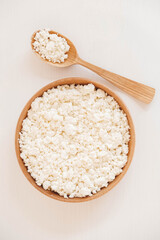 Cottage cheese in a wooden plate with a spoon on a white background