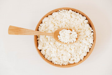Cottage cheese in a wooden plate with a spoon on a white background