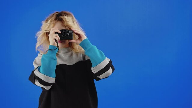 Blonde teenage girl taking picture with film camera. Blue screen studio background