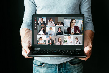 Group video chat. Business coaching. Distance education. Man holding laptop with people watching online webinar on screen in virtual class isolated on black.