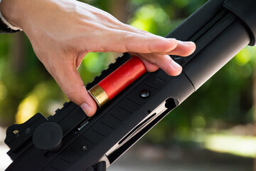 A shotgun shooter is loading a shot into the barrel of a long shotgun.