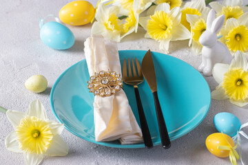 Easter table setting with daffodils, bunny, yellow and blue eggs on light gray table, Close up