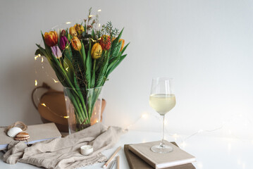 Still life with a bouquet of colorful spring tulips and a glass of white wine on the work desk.