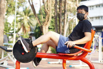 Asian man wears black face mask is exercising on spinning bike at the outdoor park. Concept: Healthcare, self protecting from coronavirus or Covid-19. Self awareness when using public park.           