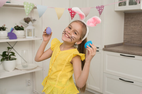a happy girl with long blonde hair in the image of an Easter bunny holds decorated eggs in her hands, looking at the camera smiling, happy Easter at home.
