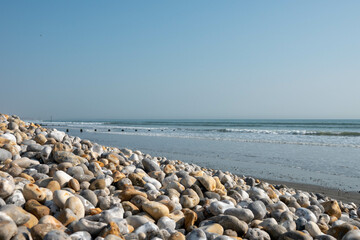 bank of pebbles with the sea and beach in the background
