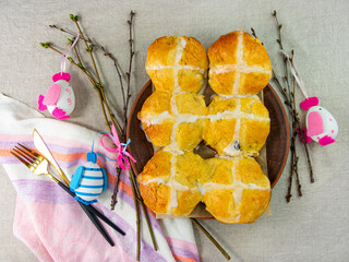 Hot cross buns on plate linen cloth tree branches Easter eggs on table top view. Fresh baked...