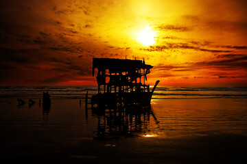 decaying metal and oil shipwreck on sand at sunset