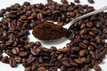 A spoon of ground coffee next to coffee beans on a white background. Roasted coffee beans. tonic...