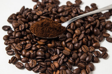 A spoon of ground coffee next to coffee beans on a white background. Roasted coffee beans. tonic...