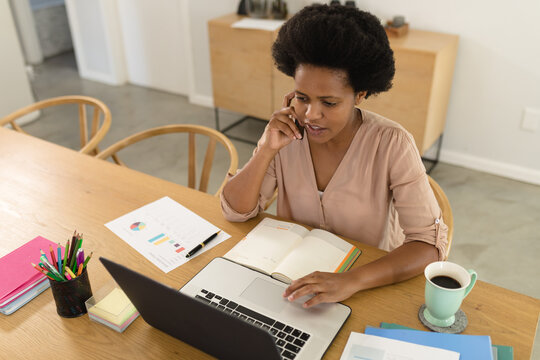 Mid adult african american female freelancer using laptop and talking on mobile phone at desk