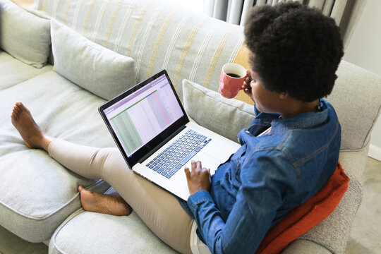 Mid adult african american female freelancer working on laptop on sofa at home