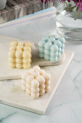 Three bubble candles - off-white, beige-colored and blue - on marble board on pale blue surface