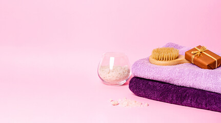 Terry bath towels with body care products on a pink background.