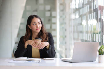 Business woman in office holding hot coffee cup looking outside thinking and imagining success.