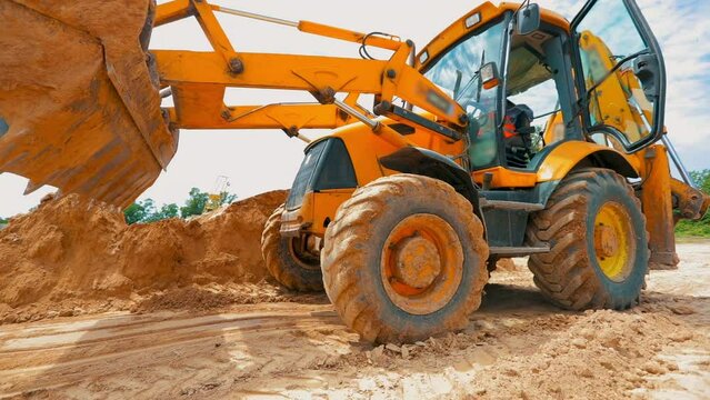 A large yellow excavator is driving on a construction site. Excavator wheels close up