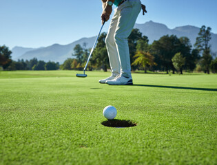 This is going to be in. Low angle shot of a unrecognizable man hitting a golfball into a hole on a golf course.