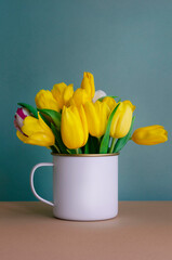 Spring beautiful background with yellow flowers tulips in a white mug. Floral background with a bouquet on the table. 